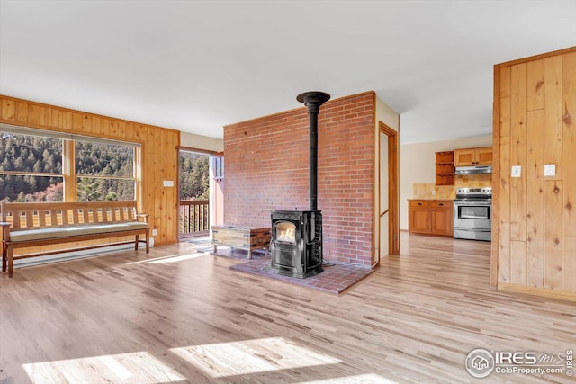 unfurnished living room with light wood-style flooring, wood walls, and a wood stove