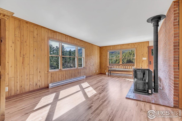 unfurnished living room with wooden walls, baseboard heating, wood finished floors, and a wood stove