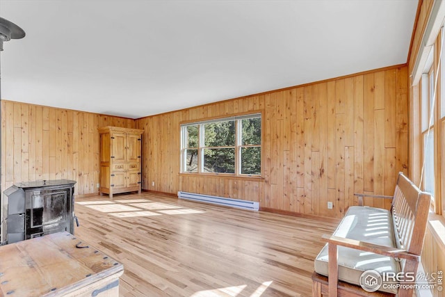 unfurnished living room with a baseboard heating unit, a wood stove, light wood-type flooring, and wood walls