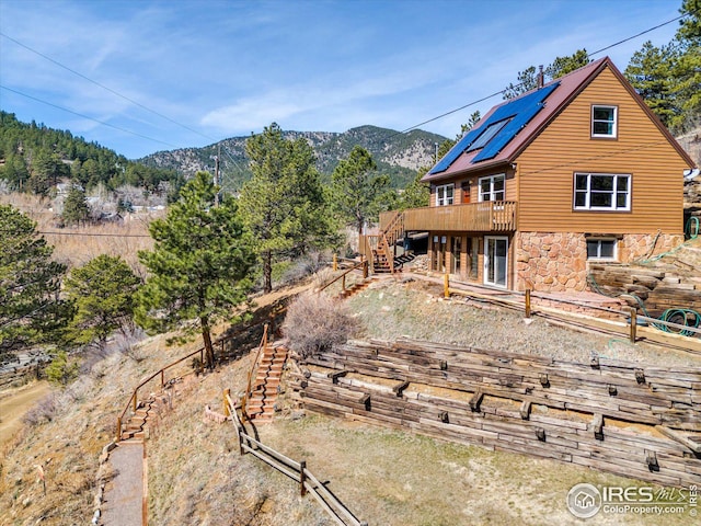 back of property featuring stairway, stone siding, a deck with mountain view, and solar panels