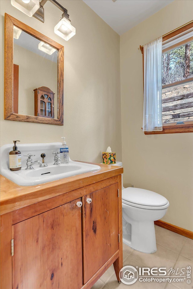 half bathroom featuring tile patterned flooring, toilet, vanity, and baseboards