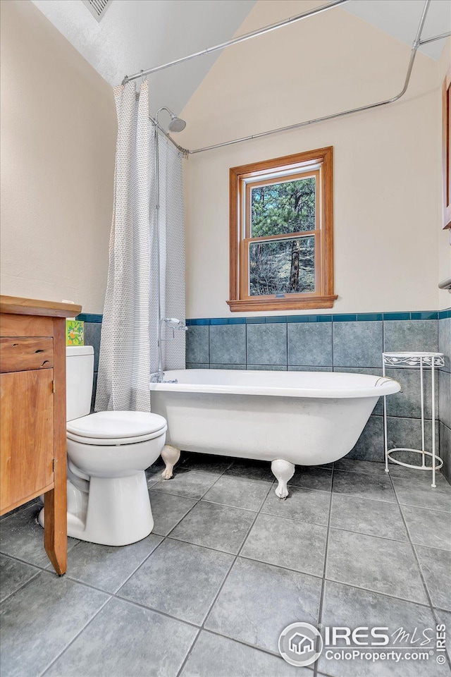 bathroom with tile walls, a wainscoted wall, tile patterned flooring, and toilet