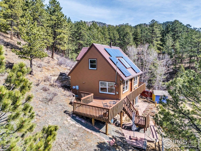 rear view of property featuring solar panels, a view of trees, stairway, and a deck