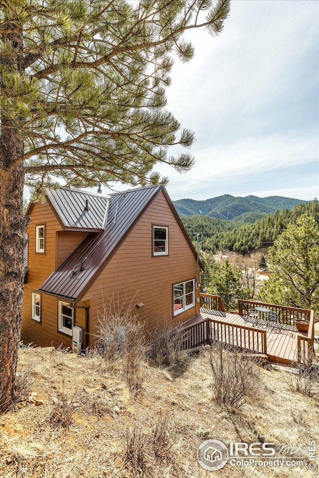 view of property exterior featuring a standing seam roof, a deck with mountain view, and metal roof