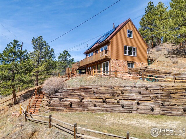 rear view of house with stone siding, stairs, a deck, and fence