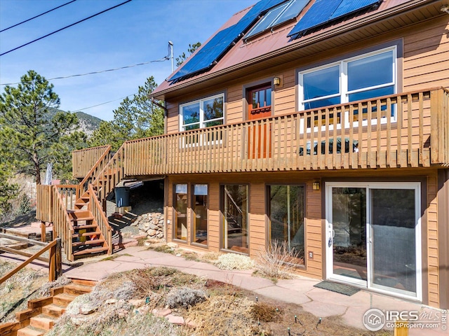 rear view of property featuring roof mounted solar panels, a deck, stairway, and metal roof