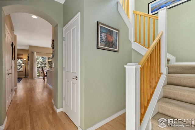 hall featuring stairs, light wood-style floors, arched walkways, and baseboards