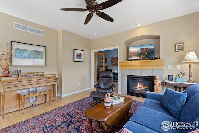 living room with visible vents, baseboards, a tile fireplace, wood finished floors, and a ceiling fan