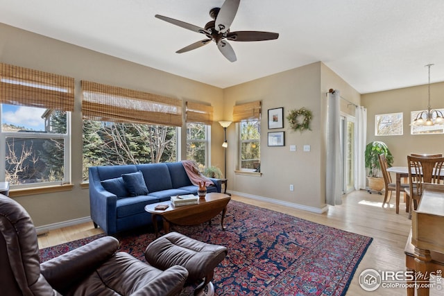 living room with ceiling fan with notable chandelier, wood finished floors, and baseboards