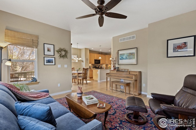 living room with a ceiling fan, light wood-style flooring, baseboards, and visible vents