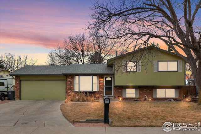 tri-level home featuring a front lawn, an attached garage, brick siding, and driveway