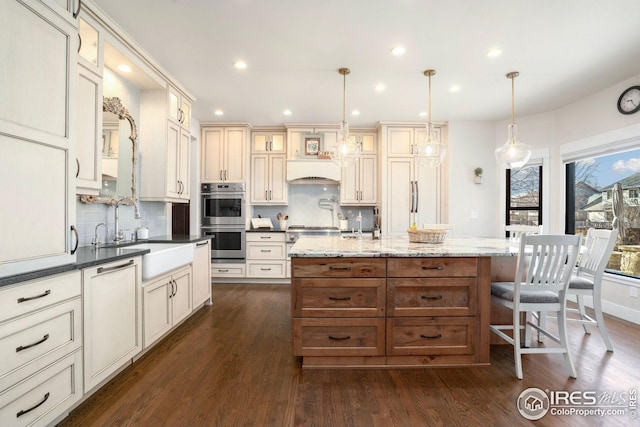 kitchen with stainless steel double oven, a kitchen island with sink, a sink, dishwasher, and tasteful backsplash