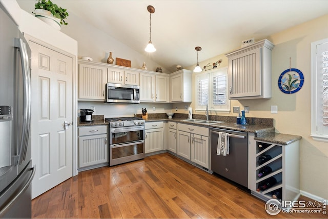 kitchen with pendant lighting, a sink, appliances with stainless steel finishes, dark wood-style flooring, and vaulted ceiling