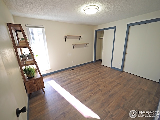 unfurnished bedroom with visible vents, multiple closets, a textured ceiling, wood finished floors, and baseboards