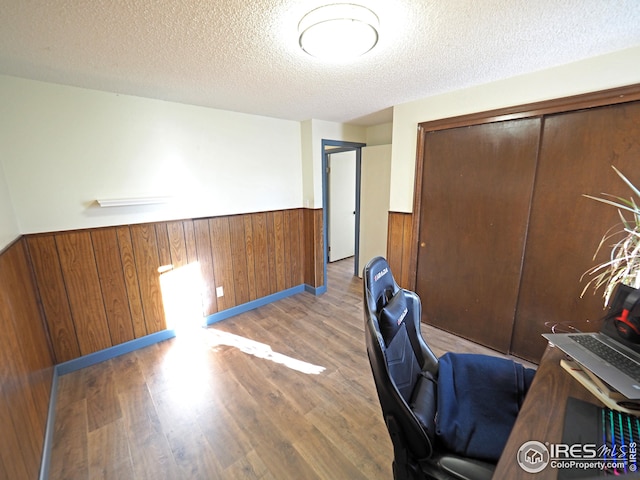 office featuring a textured ceiling, wooden walls, wood finished floors, and wainscoting