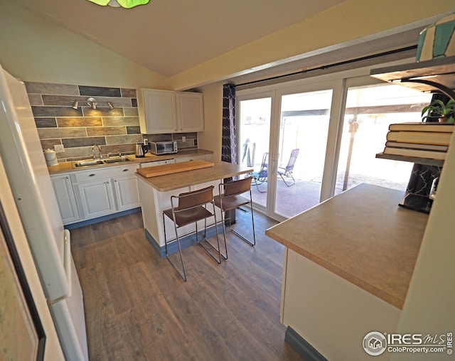 kitchen with lofted ceiling, dark wood-style flooring, a sink, white cabinets, and backsplash