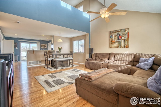 living area featuring visible vents, baseboards, a high ceiling, light wood-style floors, and a ceiling fan