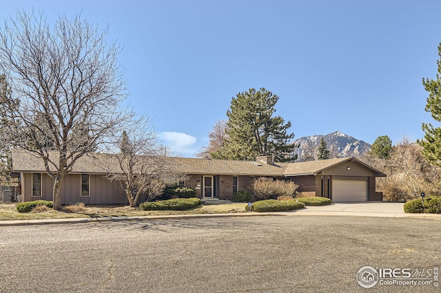 ranch-style house with brick siding, a chimney, concrete driveway, a garage, and a mountain view