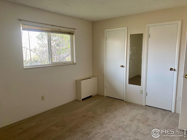 unfurnished bedroom featuring a textured ceiling, radiator, and light carpet