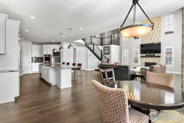 dining space with stairs, recessed lighting, baseboards, dark wood-style flooring, and a tile fireplace