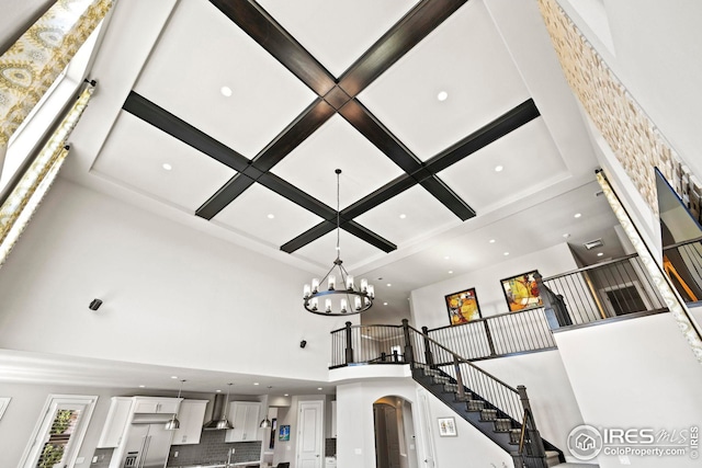 interior details with coffered ceiling, recessed lighting, arched walkways, wall chimney exhaust hood, and a chandelier