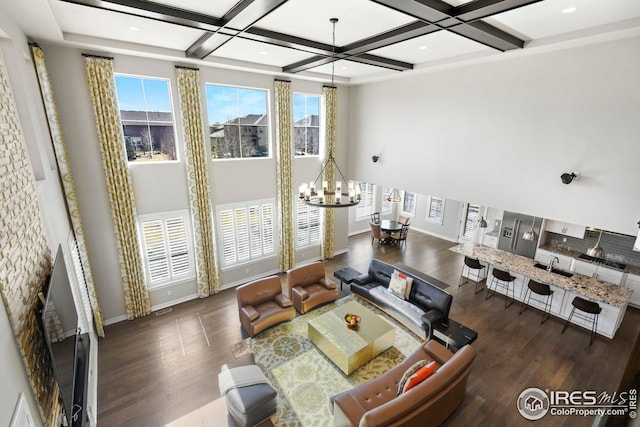 living room with a notable chandelier, coffered ceiling, wood finished floors, a high ceiling, and baseboards