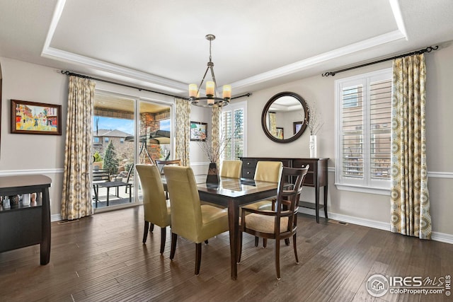 dining room featuring baseboards, dark wood finished floors, ornamental molding, a raised ceiling, and a chandelier