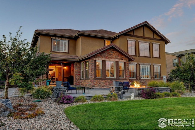 rear view of house with stucco siding, stone siding, a patio, an outdoor fire pit, and a yard