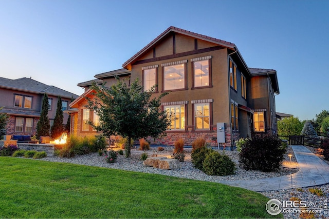 view of side of property featuring fence, an outdoor fire pit, stucco siding, stone siding, and a lawn