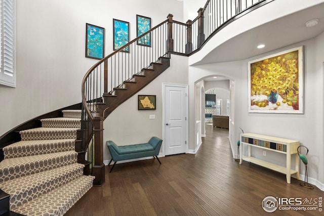 foyer featuring wood finished floors, baseboards, a high ceiling, arched walkways, and stairs