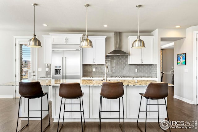 kitchen with stainless steel built in fridge, dark wood-type flooring, wall chimney exhaust hood, and white cabinetry