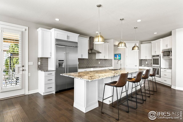 kitchen featuring built in appliances, dark wood-style floors, white cabinets, wall chimney exhaust hood, and a sink