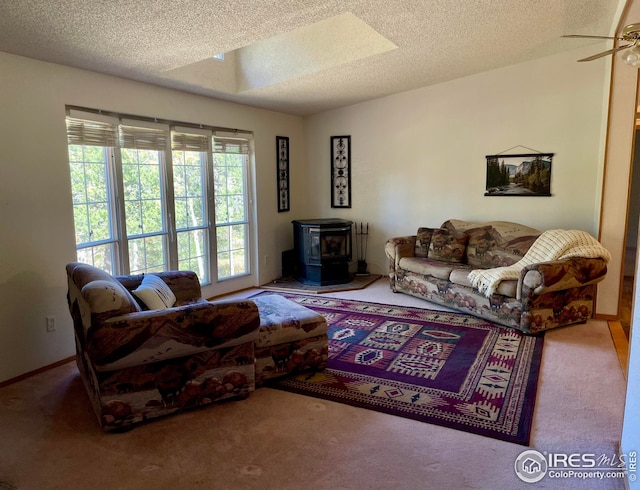 carpeted living room with a wood stove, a skylight, a ceiling fan, and a textured ceiling