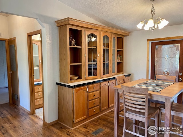 dining room with visible vents, dark wood-type flooring, a notable chandelier, a textured ceiling, and lofted ceiling