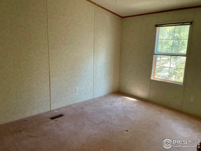 carpeted spare room with a wealth of natural light, visible vents, a textured ceiling, and ornamental molding