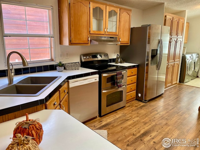 kitchen featuring under cabinet range hood, light wood-style flooring, appliances with stainless steel finishes, separate washer and dryer, and a sink