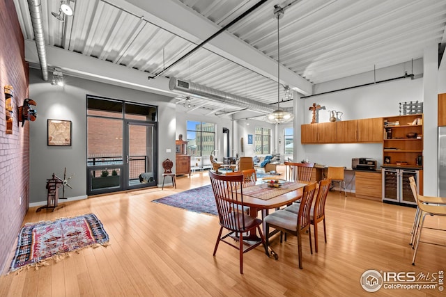dining room with beam ceiling, beverage cooler, light wood-type flooring, and brick wall
