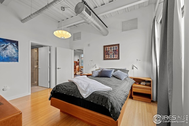 bedroom with light wood-style flooring, beamed ceiling, visible vents, and a towering ceiling