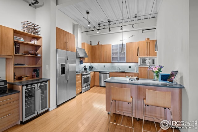 kitchen with a sink, stainless steel appliances, wine cooler, light wood-style floors, and a towering ceiling