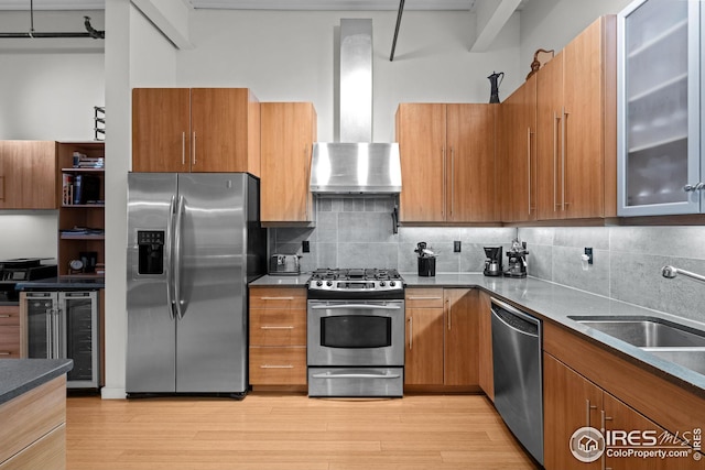 kitchen with brown cabinetry, beverage cooler, light wood finished floors, stainless steel appliances, and wall chimney exhaust hood