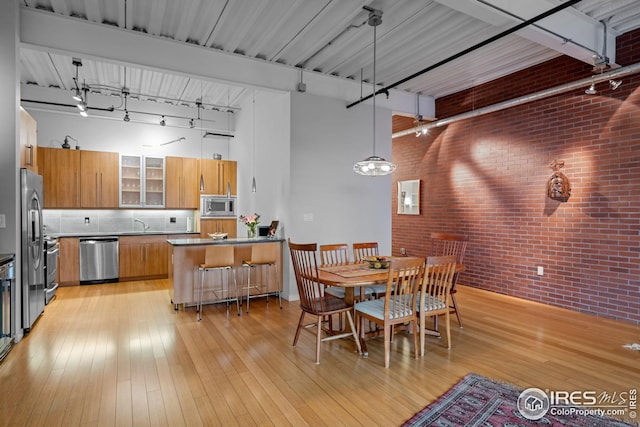 dining room with brick wall, rail lighting, light wood-type flooring, and a towering ceiling