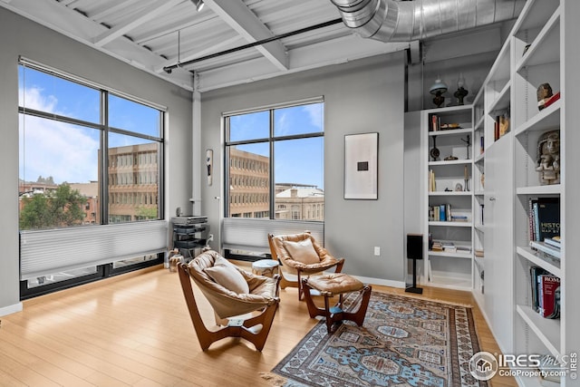 sitting room with electric panel, beamed ceiling, a healthy amount of sunlight, and wood finished floors