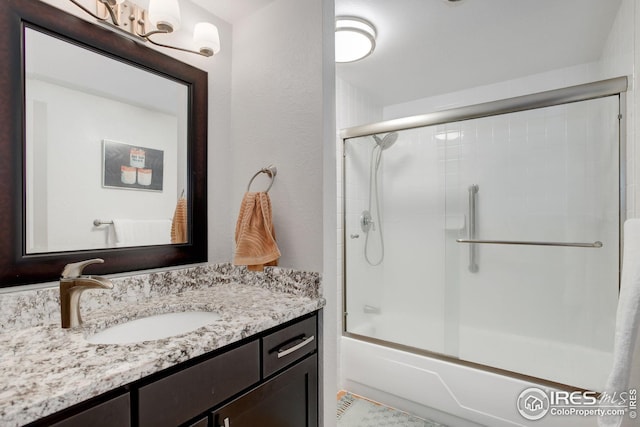 bathroom with vanity, a textured wall, and bath / shower combo with glass door