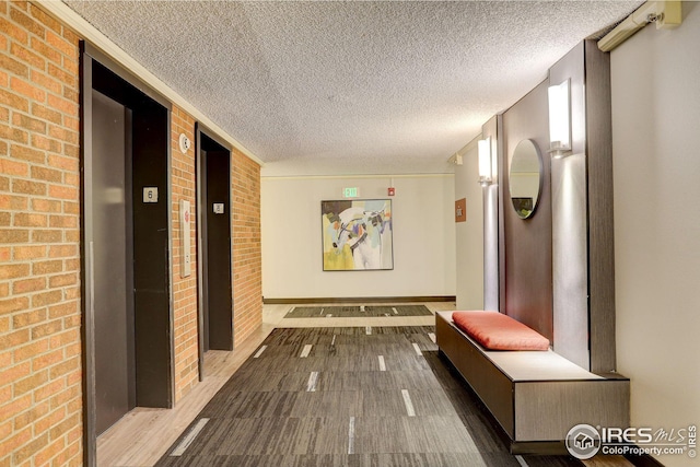 corridor featuring elevator, brick wall, a textured ceiling, and wood finished floors