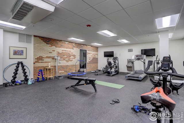 workout area featuring a drop ceiling, visible vents, and brick wall