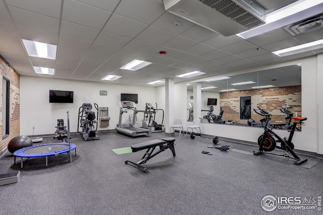 exercise room with visible vents, brick wall, a paneled ceiling, and baseboards