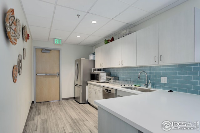 kitchen with a sink, backsplash, stainless steel appliances, light wood-style floors, and light countertops