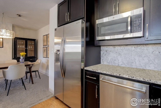 kitchen featuring tasteful backsplash, pendant lighting, light wood-type flooring, light stone counters, and appliances with stainless steel finishes