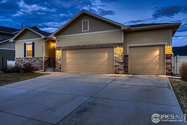 craftsman-style house with stone siding, an attached garage, concrete driveway, and fence