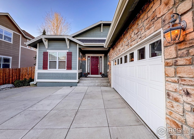 exterior space with stone siding, driveway, a garage, and fence